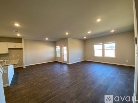 A spacious room with wooden floors and a kitchen area to the left.