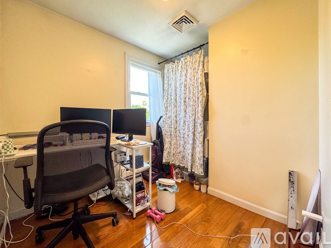 A room with a desk, computer, chair, and a window with curtains.