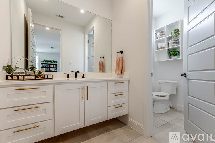 A white bathroom with a vanity and a toilet in the background.