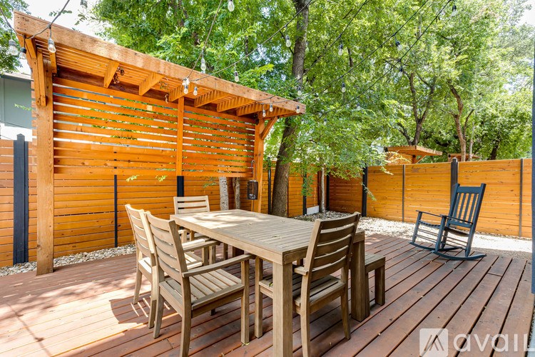 A wooden table and chairs are set up on a deck with a pergola.