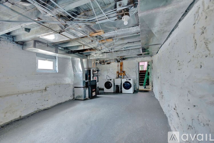 A room with a concrete floor and walls, featuring a window, a staircase, and two air conditioning units.