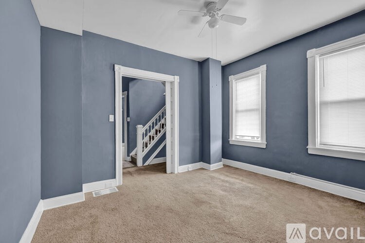 A room with a carpeted floor, a ceiling fan, and a staircase leading to another room.