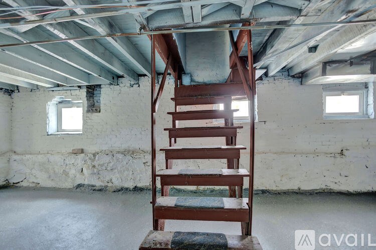 A wooden staircase in a room with exposed ceiling beams and two windows.