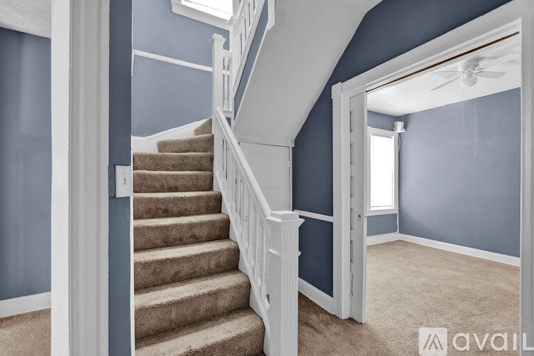 A staircase with a beige carpeted runner and white balusters leads to a landing with a ceiling fan.