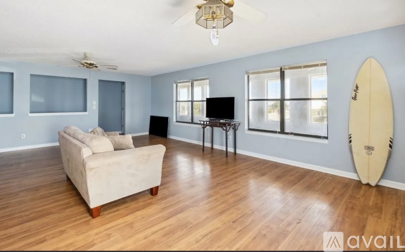 A living room with a couch, a television, and a surfboard leaning against the wall.