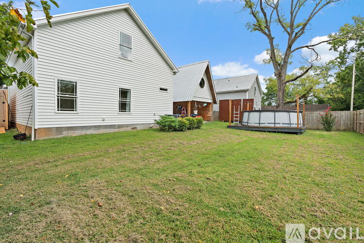 A house with a white exterior and a brown roof is surrounded by a fence and a tree.