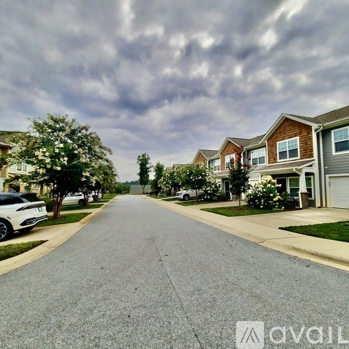 A street view of a residential area with houses on both sides and cars parked along the curb.