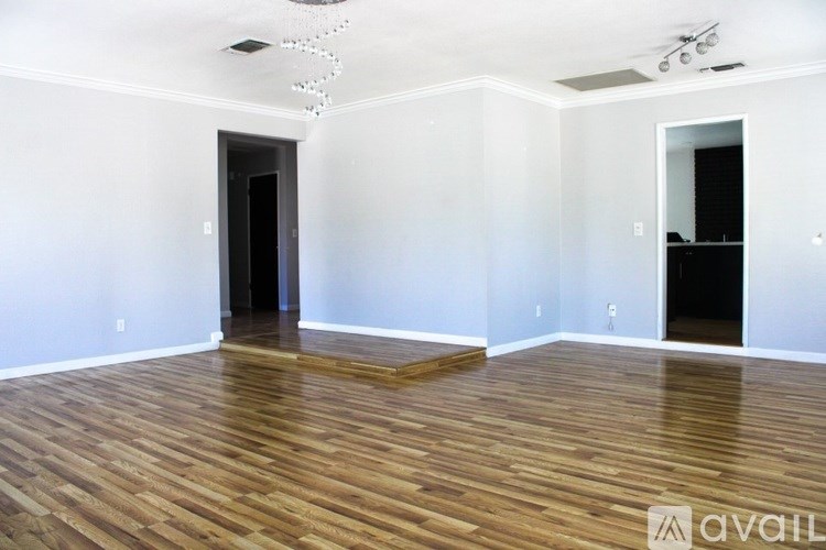 A room with wooden floors and white walls, with a chandelier hanging from the ceiling.