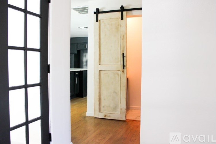 A white door with a black handle is open to a room with a wooden floor.