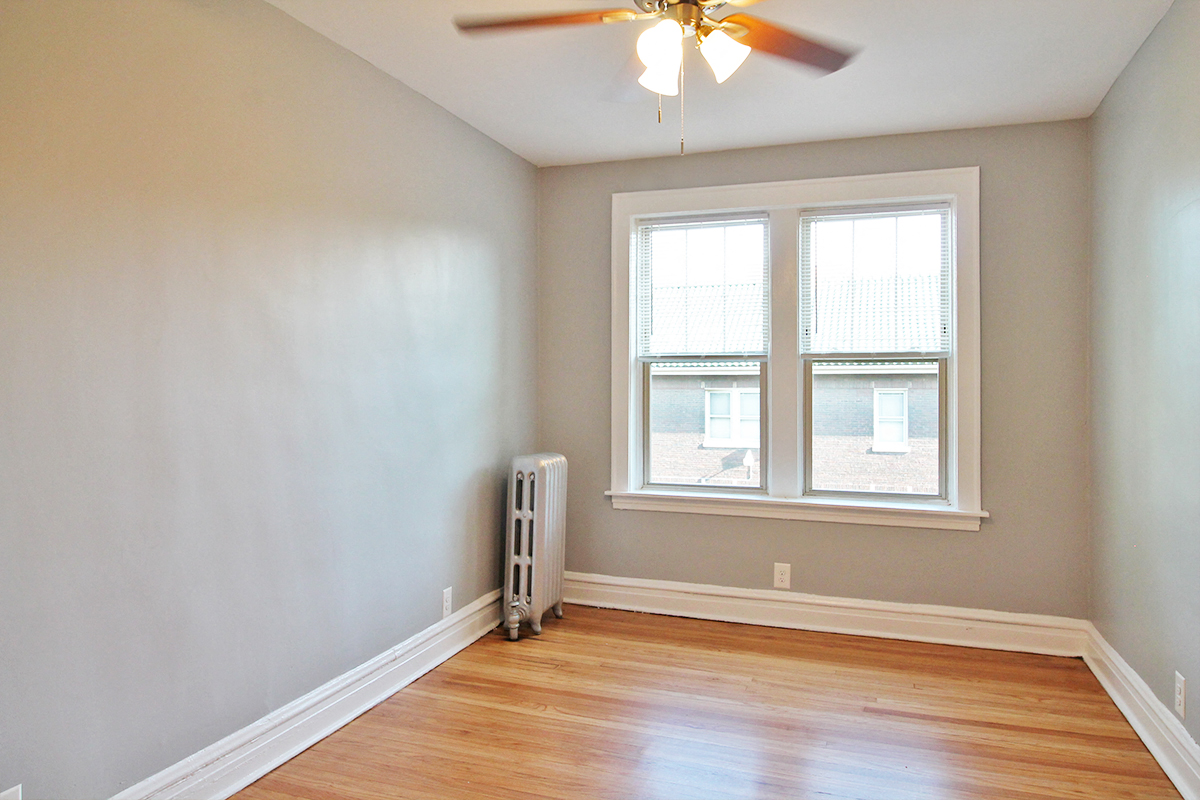an empty room with a ceiling fan and two windows