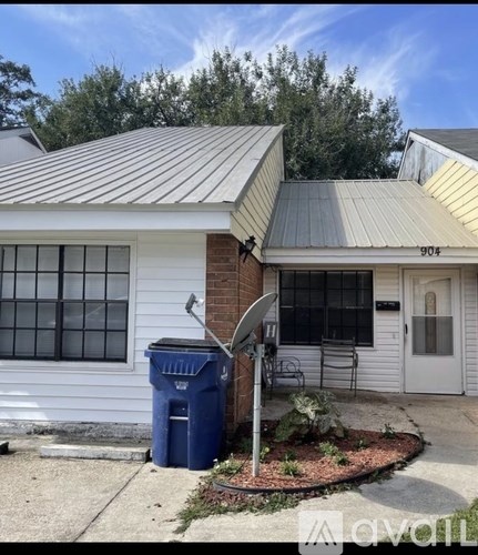 A white house with a blue trash bin in front.