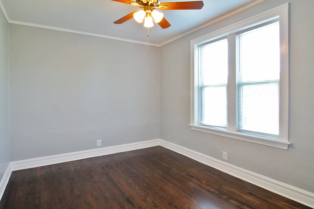 an empty room with a ceiling fan and two windows