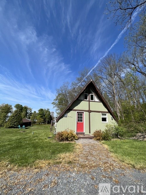 A small house with a red door is surrounded by a grassy area and trees.