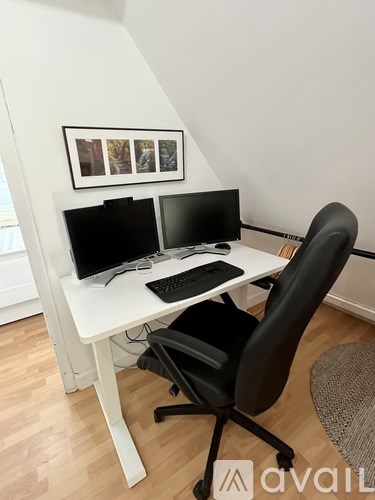 A white desk with a black chair and two monitors on it.