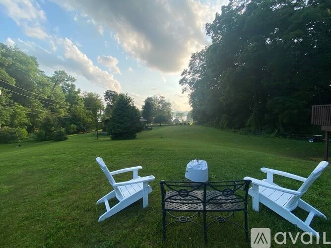 Two white chairs are placed on a lawn with a table between them.