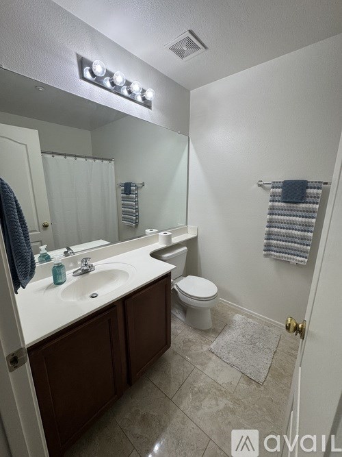 A bathroom with a white sink, toilet, and a mirror with lights above it.