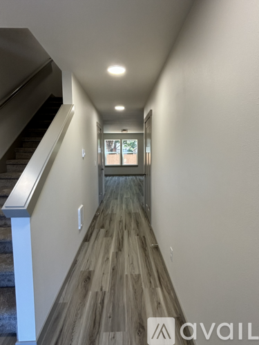 A hallway with wood flooring and a staircase on the left side.