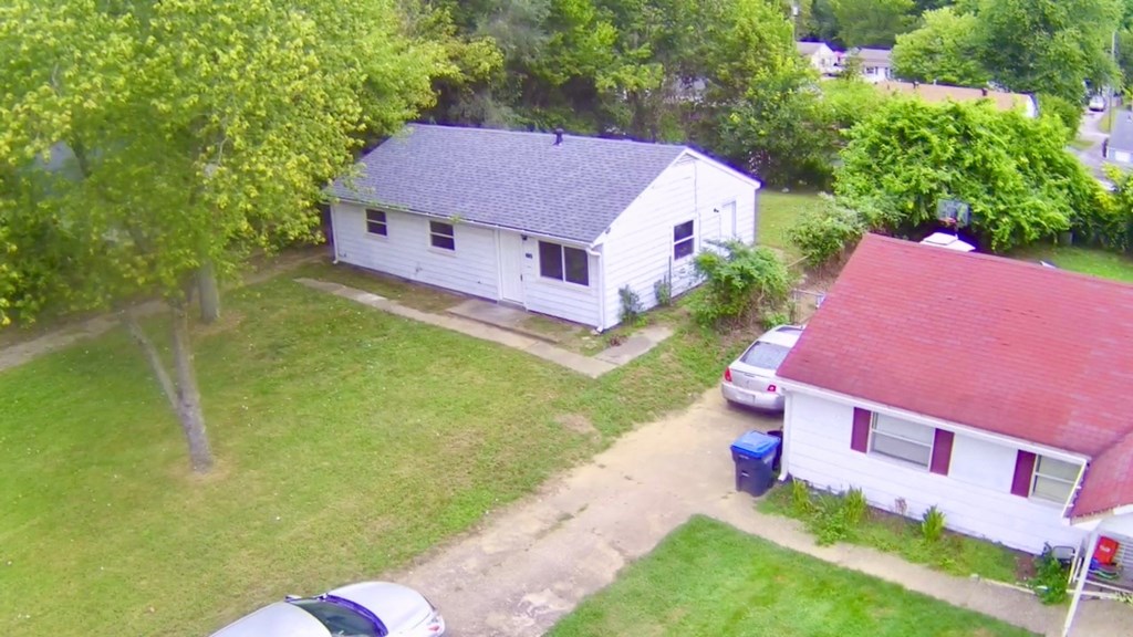 A white house with a red roof is surrounded by green grass and trees.