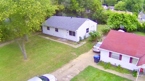 A white house with a red roof is surrounded by green grass and trees.