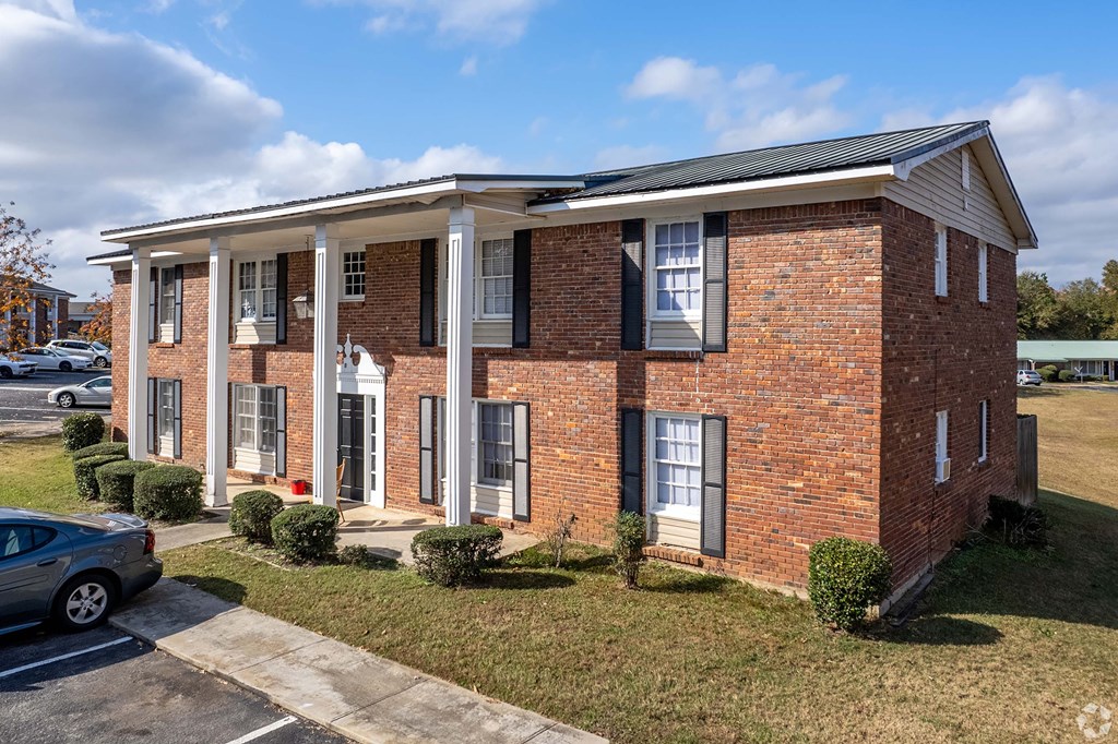 A red brick residential building with columns and a car parked in front.