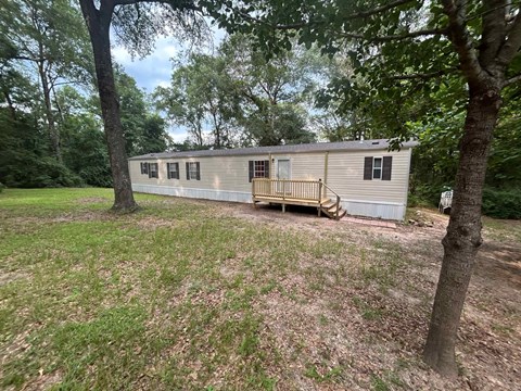 A mobile home sits in a grassy area with trees in the background.