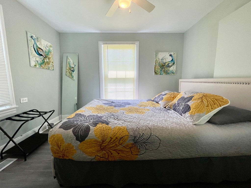 A bedroom with a bed, a fan, and two wall art pieces.
