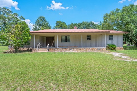 A house with a red roof and white walls is surrounded by a grassy lawn.