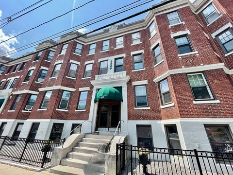 A red brick building with a green awning and a black fence in front.