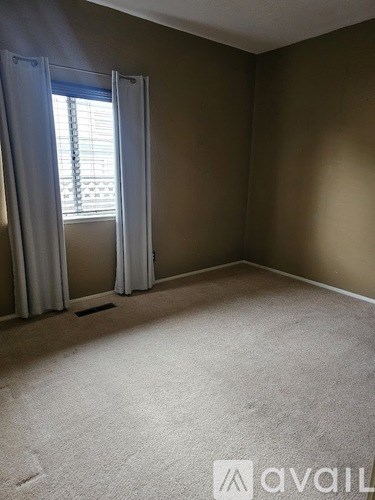 A room with a carpeted floor and a window with curtains.