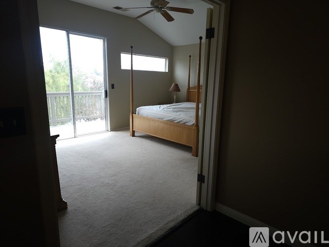 A bedroom with a bed, a ceiling fan, and a sliding glass door leading to a balcony.