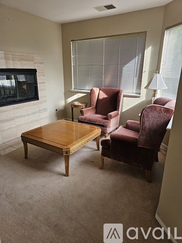 A living room with a fireplace, two chairs and a table.