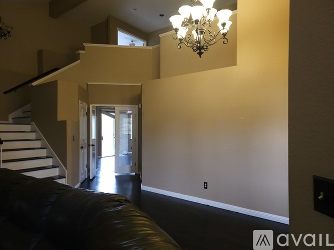 A living room with a black leather couch and a chandelier.