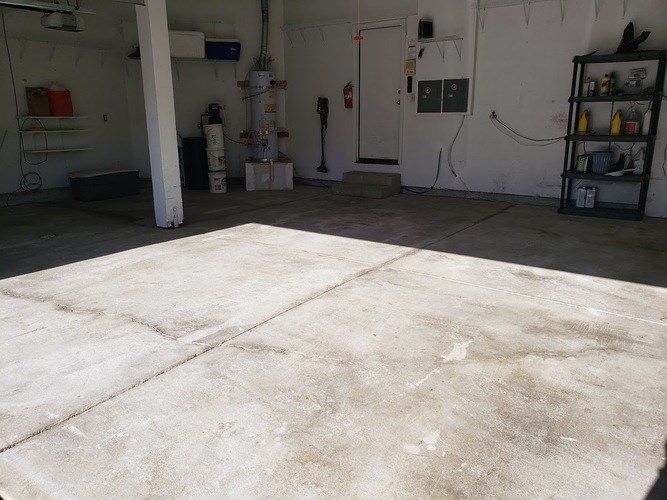 A large concrete floor in a garage with a fire extinguisher and a shelf with tools.