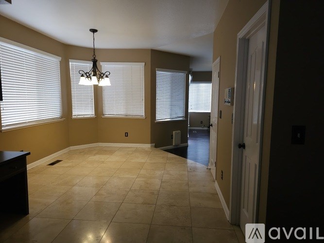 A room with a chandelier, tiled floor, and a door leading to another room.