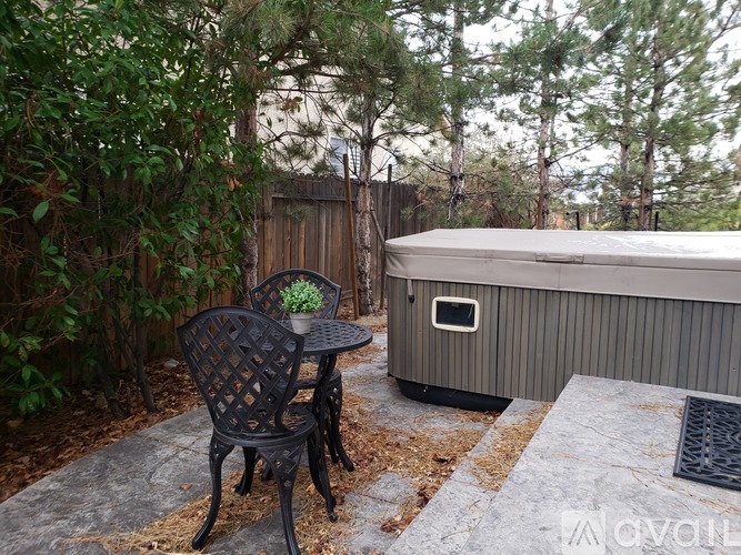 A hot tub sits on a patio with a black chair and table.