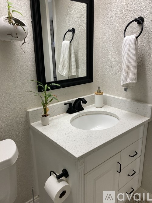 A bathroom with a white counter top and a black mirror.
