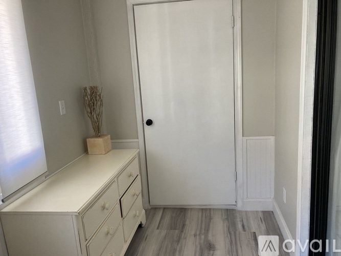 A white dresser with a plant on top and a white door.