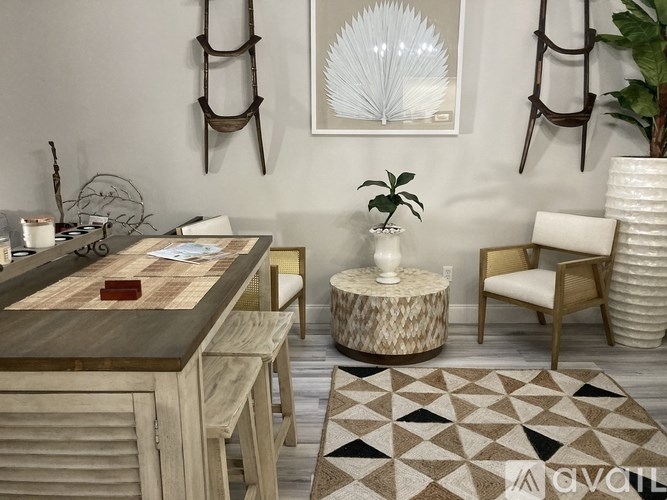 A living room with a wooden table and chairs, a plant, and a rug.