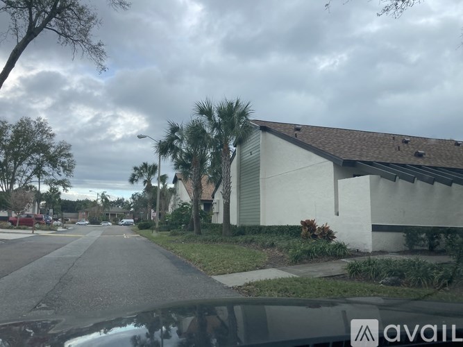 A street view with a car in the foreground and a house with a white exterior and a brown roof.