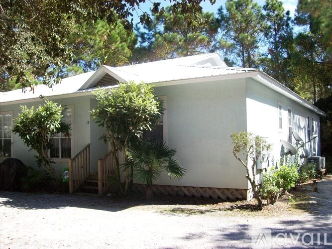 A white house with a porch and a tree in front.