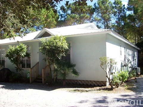 A white house with a porch and a tree in front.
