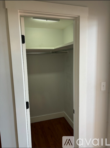 A white door with a black handle is open to a small, empty room with a wooden floor.