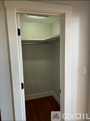 A white door with a black handle is open to a small, empty room with a wooden floor.