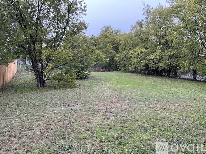 A grassy backyard with trees and a fence.