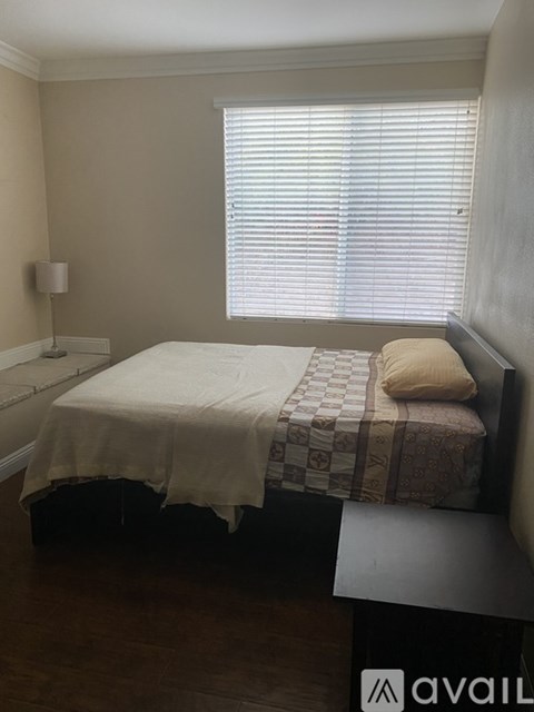 A bedroom with a bed, a nightstand, and a window with blinds.