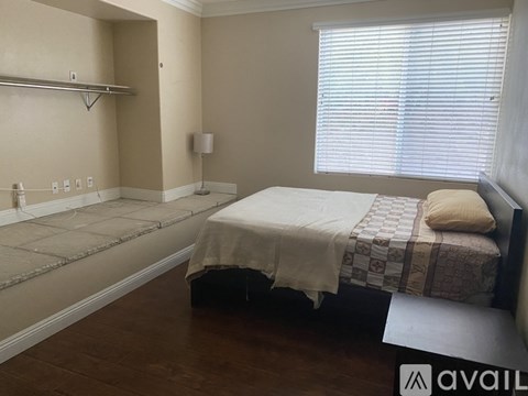 A bedroom with a bed, a small table, and a window with blinds.