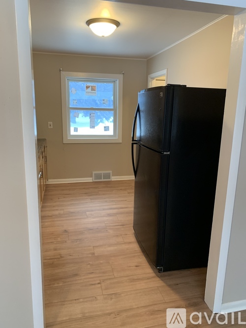 A black refrigerator in a room with wooden flooring and a window.