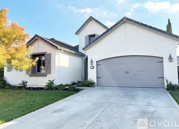 A white house with a grey garage door and a tree with yellow leaves in front.
