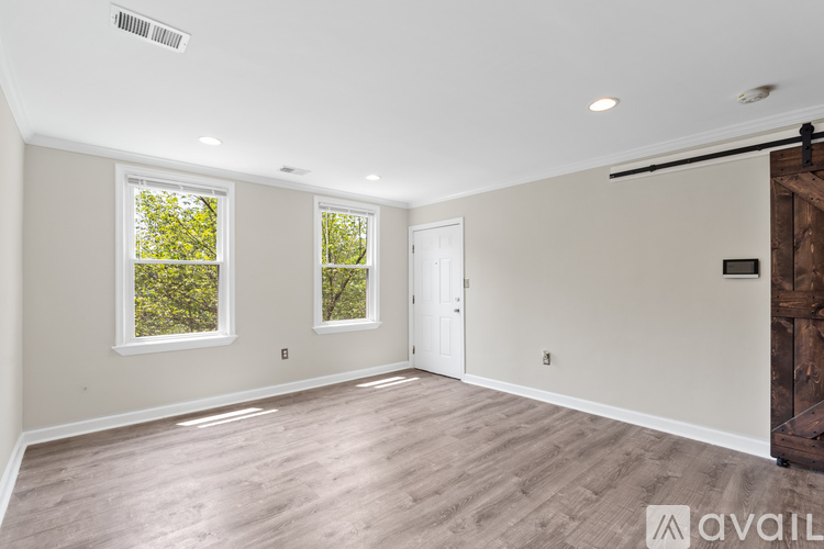 A spacious room with wooden flooring and two windows.