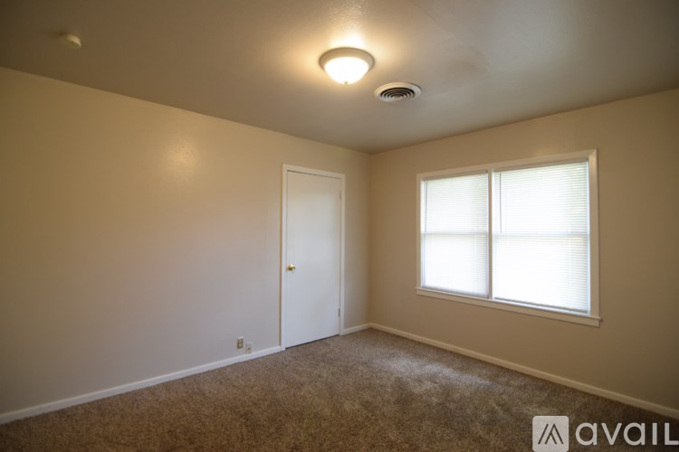 A room with a carpeted floor, a window with blinds, a door, and a ceiling light fixture.
